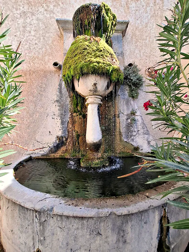Une fontaine couverte de mousse dans une rue de Moustiers