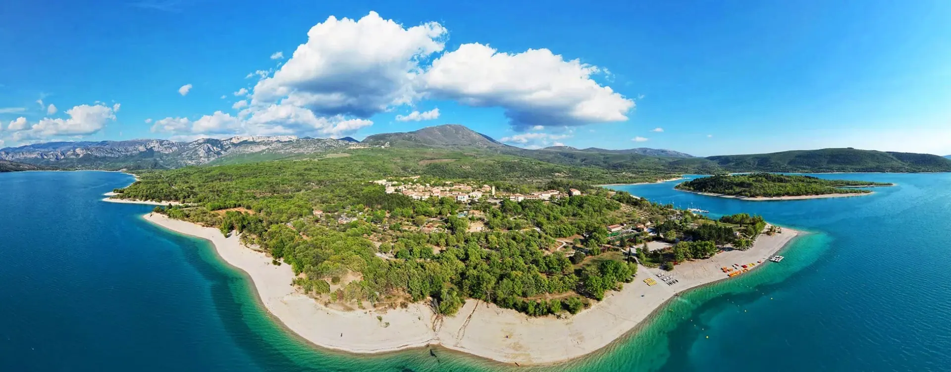 Vue aérienne des Salles-sur-Verdon : le village dans les arbres, ses plages de galets et le lac de Sainte-Croix